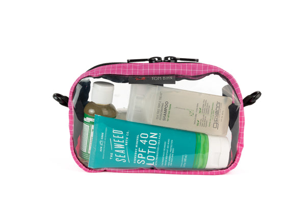 A Cerise (pink with white grid pattern) Halcyon 3D Clear Organizer Cube filled with sundries.